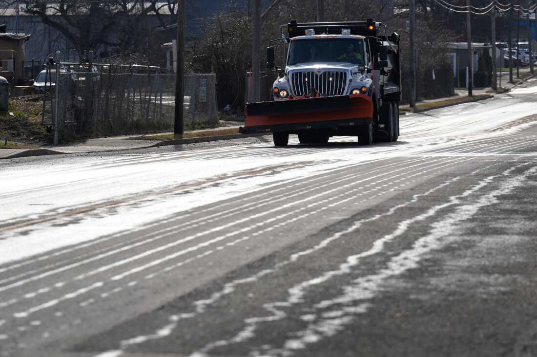 A truck with a snowplow on the front applies salt brine to a road.