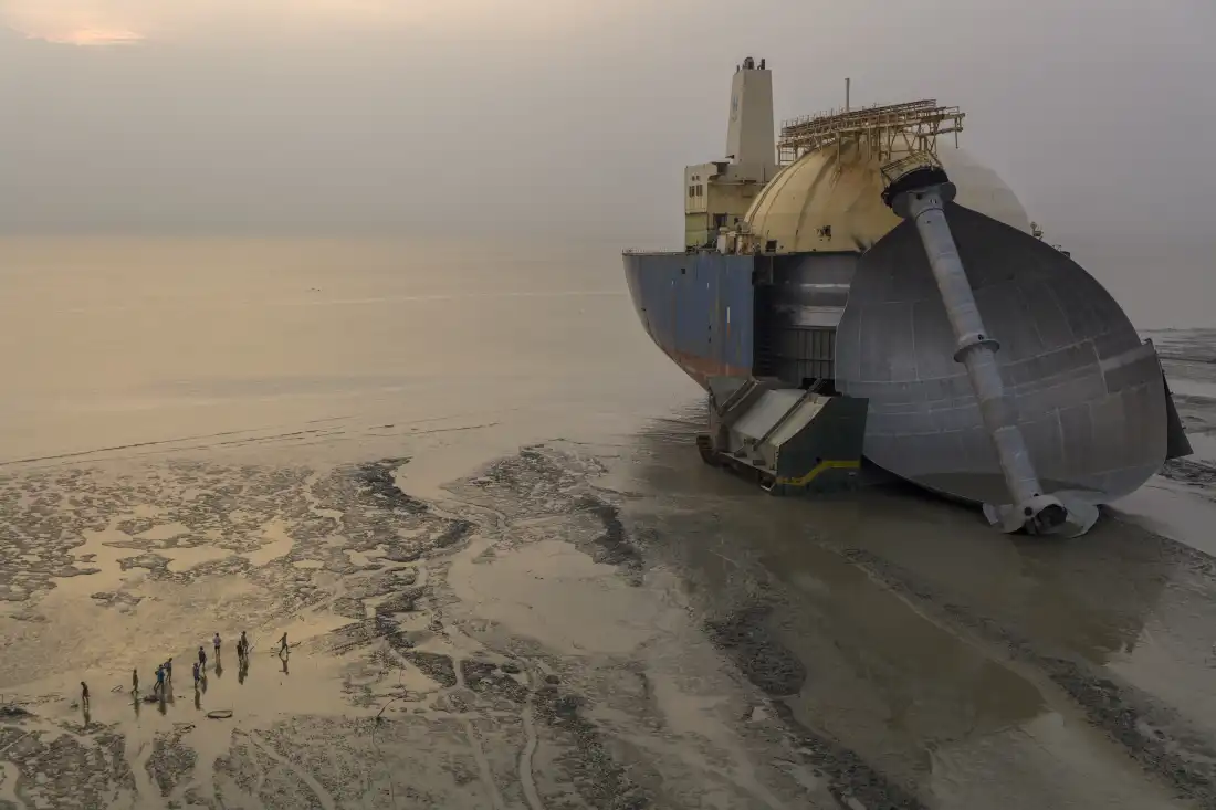 An old LNG carrier in the final stage of disassembly for scrap metal on the mudflats of the Bay of Bengal, just north of Chattogram, Bangladesh. Breaking a ship like this will take about a year, with a crew of 60 men using blow torches and winches to drag the larger pieces ashore for cutting into smaller pieces. The nearby BSRM smelter melts down the scrap metal from the old boats and produces rebar and rolled steel, while the more valuable non-ferrous metals are sold overseas. The brass from this ship was sold to Hyundai, the ship’s manufacturer in Korea, for use in new ships. From this LNG ship, they will collect a total of 30k tons of metal, plus 2.4k tons of aluminum and 200-300 tons of brass, copper, and stainless steel. Bangladesh has no iron mines and relies on shipbreaking for much of its iron and steel. Shipbreaking requires low wages and high demand for scrap steel. LNG boats are more valuable as they have large quantities of non-ferrous metals that fetch higher prices. Bangladesh had 160 shipbreaking yards before the June 2025 regulation requiring that all new ship purchases after that date be broken using “green methods” requiring international certifications. This forced most of the shipbreakers out of business, and now there are only 10 active shipbreaking yards. The green regulations require a US$4-5 million investment in a thick concrete slab for breaking work, a crane, and toxic liquid storage tanks, as well as higher wages and international certifications. resulting in higher operating costs. This LNG ship was purchased before the June 2025 green deadline. The world’s biggest ship-breaking areas are in Alang, India; #2 is Bangladesh; #3 is Pakistan; and they are all now subject to the same standards. This old-style ship-breaking operation is being done in a rented yard and run by Marine Safety System, but its owner, Mr. Kamal Ahamad, doesn’t want his name or the company’s name mentioned in captions. Kamal works in Bangla