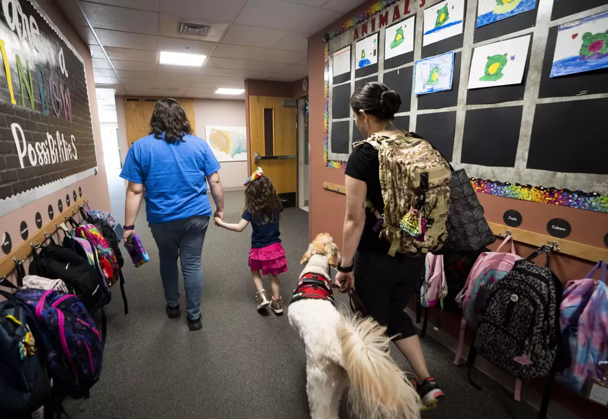 Special education teacher Vivien Henshall walks with student Scarlett Rasmussen, 8, as Scarlett's mother, Chelsea, follows with a service dog. Because of her disabilities, Scarlett needs regular access to a nurse at school.