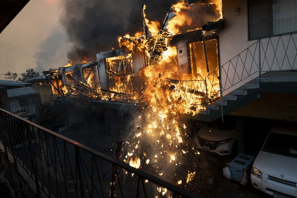In this photo, a row of apartments is engulfed in yellowish flames, and debris that's on fire is falling downward.