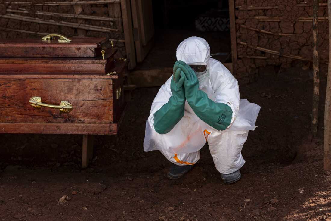 A health worker in protective equipment carries out safe burial procedures beside the coffin of a suspected Ebola victim outside a family home in Mongbwalu, Ituri province, DRC, on May 24, 2026.