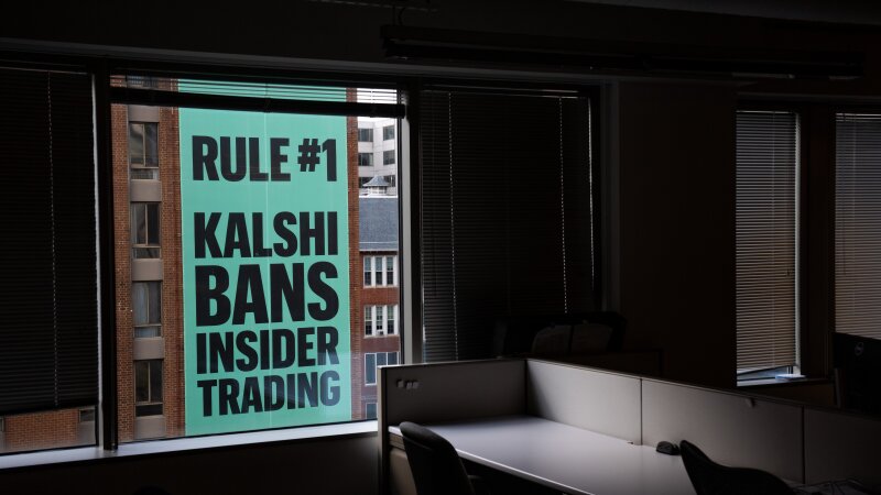 Viewed through the window of an office building, a giant banner for the prediction market platform Kalshi hangs on the outside of a building across the street on April 1. The banner says in all capital letters: "Rule #1 Kalshi bans insider trading."