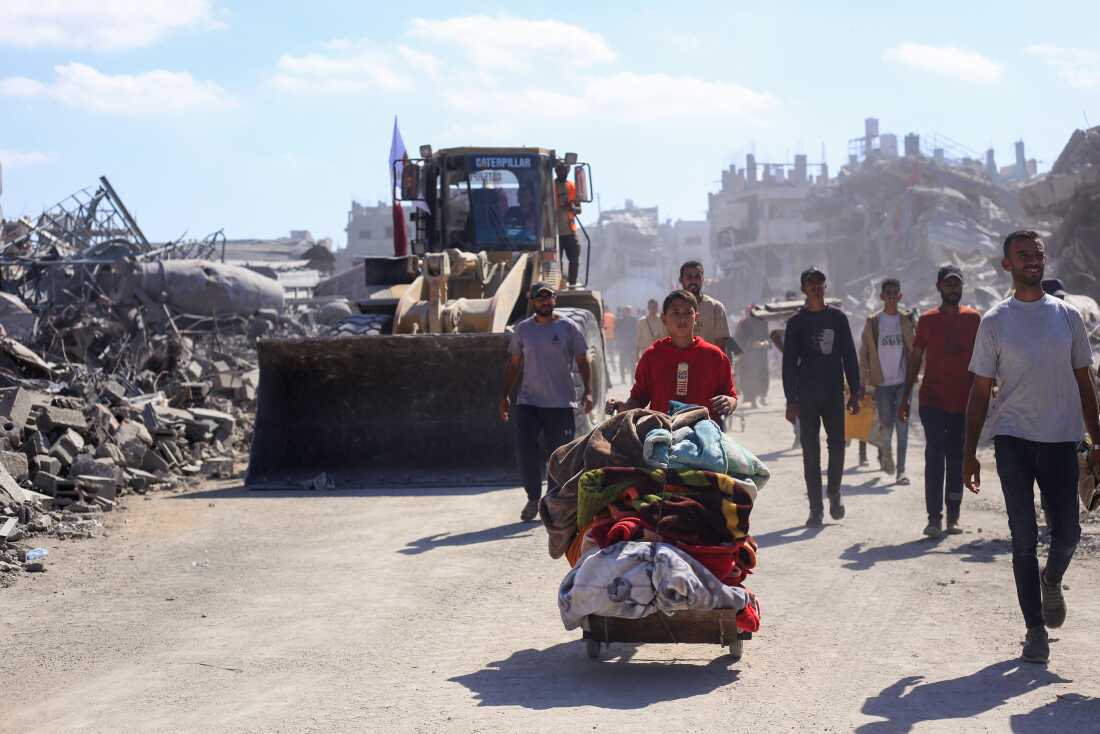 Bulldozers deployed by the Gaza Municipality drive past displaced people, on their way to clear building rubble from main roads in Gaza City, on Tuesday, amid a ceasefire between Israel and Palestinian fighters in Gaza.