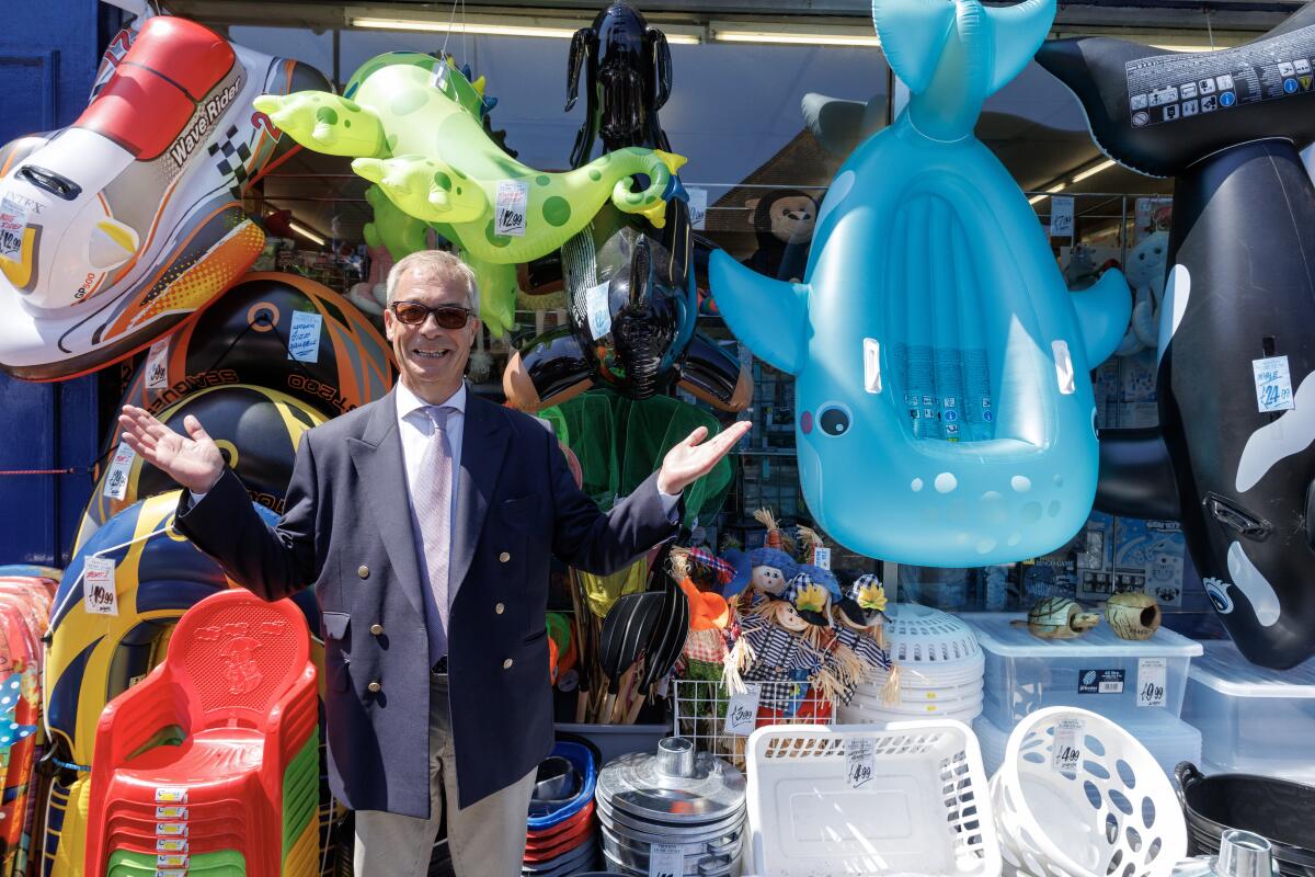 Reform UK leader Nigel Farage stops outside a bucket and spade shop for a photograph while speaking to members of the public on the High Street on July 8, 2026, in Frinton-on-Sea, England.