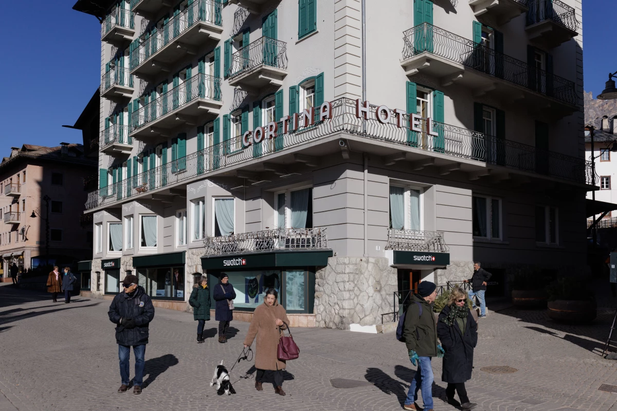Pedestrians walk past the historic Hotel Cortina and luxury retail shops in the town's central pedestrian area. As the 2026 Winter Olympics began, the contrast between Cortina's traditional Alpine charm and the increasing commercialization has become a focal point for local critics.