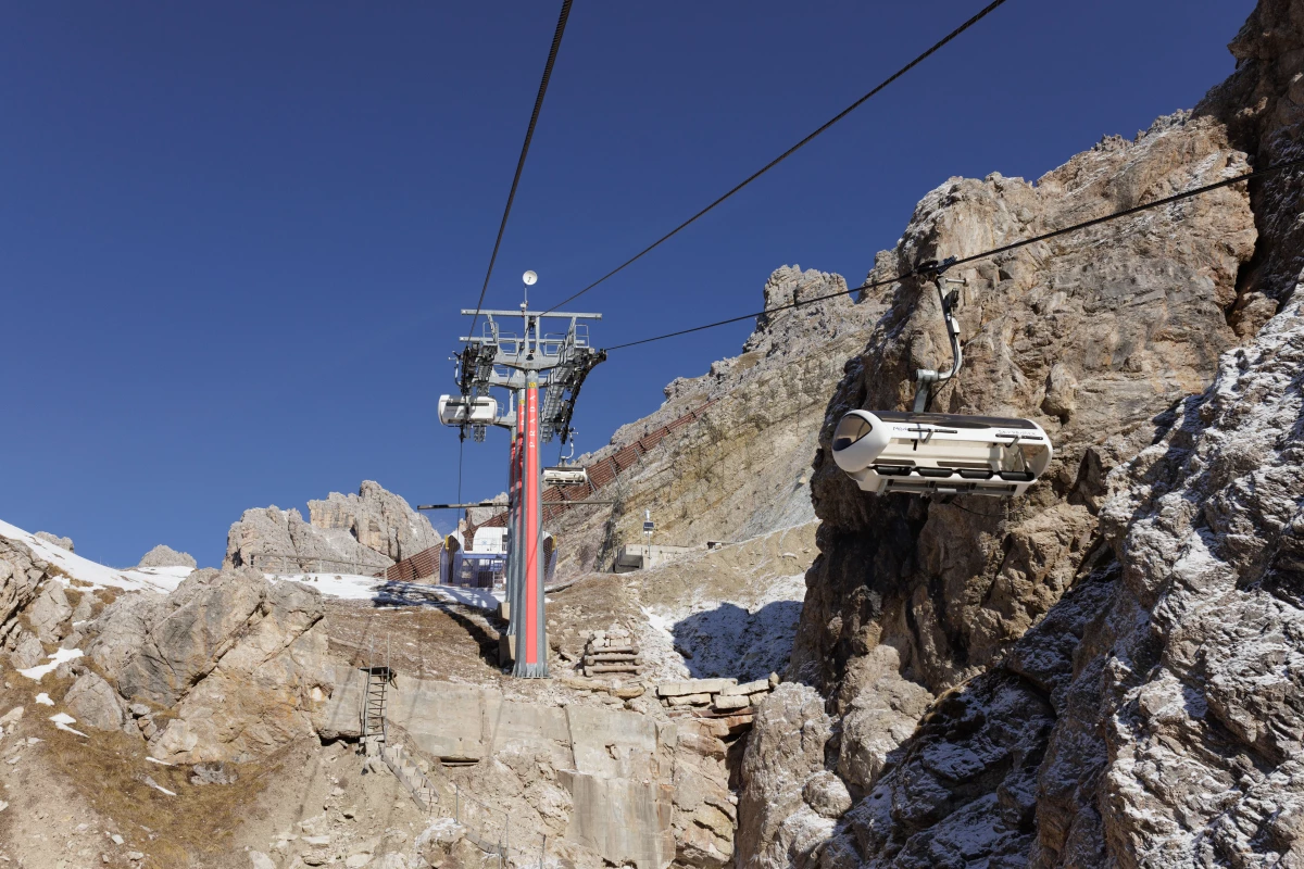 The Prada logo is prominently displayed on a pylon of the Tre Croci - Son Forca chairlift, which stands over noticeably thin snow cover on the slopes of the Cristallo massif. This image captures two major challenges facing the Winter Olympics: the increasing reliance on private luxury investment to fund infrastructure and the stark reality of climate change in the Dolomites.
