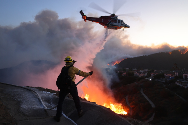 Fire personnel respond to homes destroyed while a helicopter drops water as the Palisades Fire grows on Tuesday.