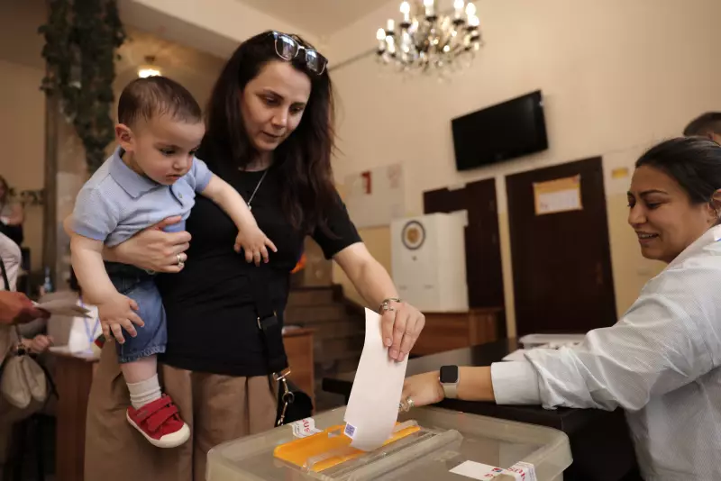 A woman holding a child casts her ballot at a polling station during a parliamentary election in Yerevan, Armenia, Sunday, June 7, 2026.