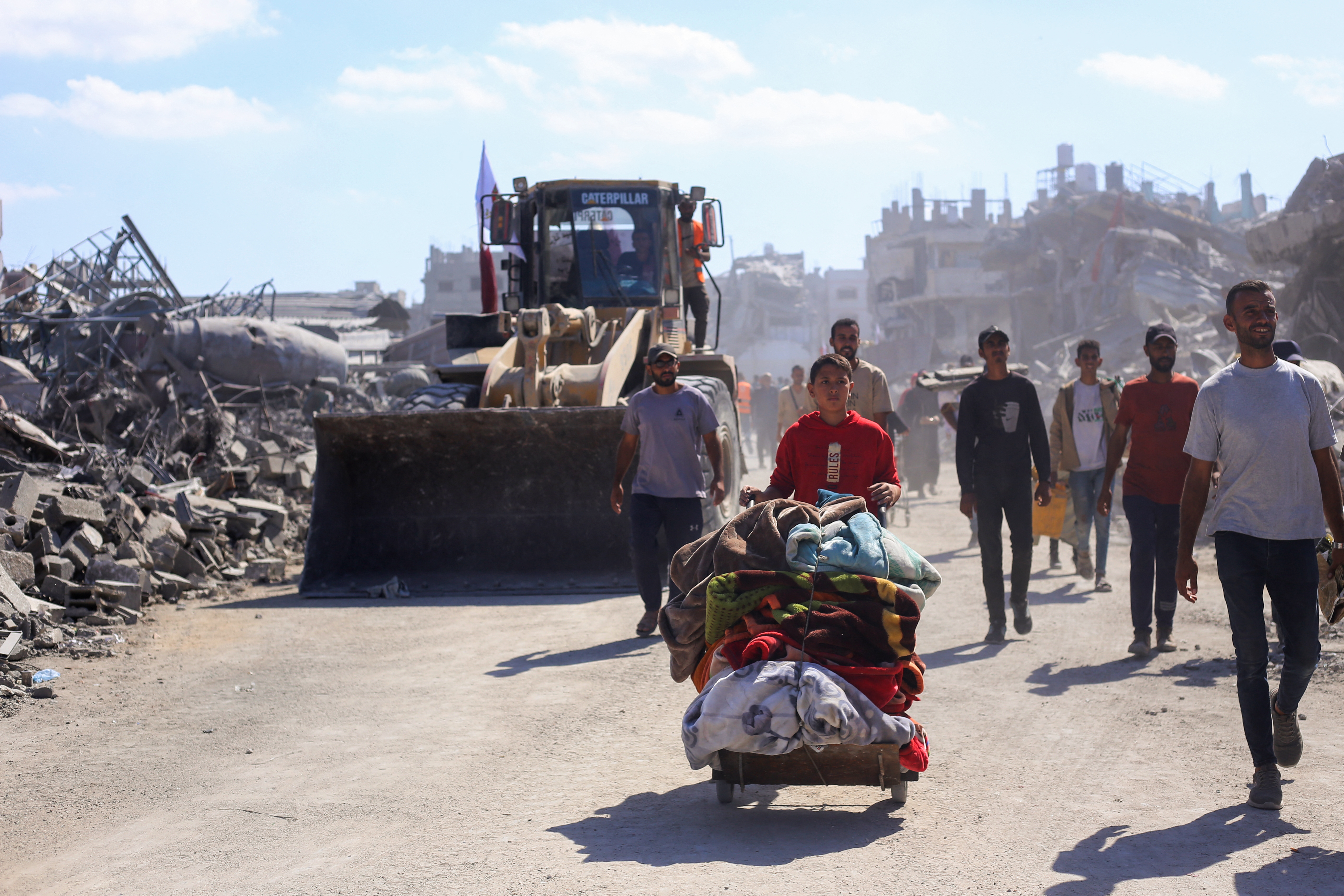Bulldozers deployed by the Gaza Municipality drive past displaced people, on their way to clear building rubble from main roads in Gaza City on Tuesday, amid a ceasefire between Israel and Palestinian fighters in Gaza.