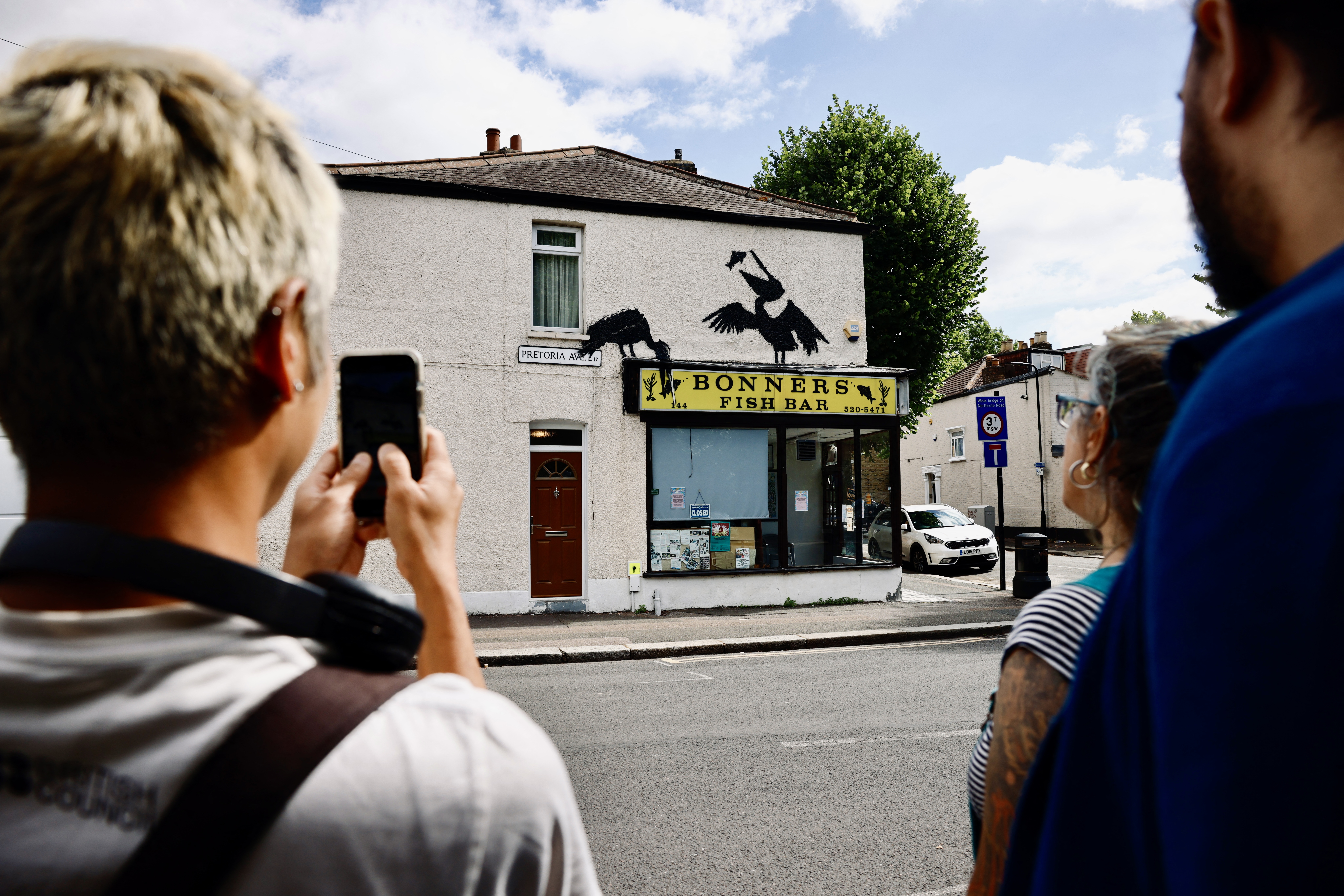 People gather to look at an artwork by street artist Banksy depicting two pelicans catching fish, painted on top of a fish-and-chips shop in Walthamstow, northeast London, on Aug. 9.