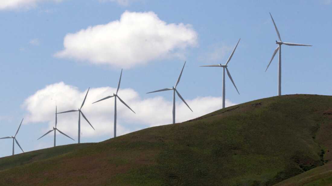 Seven modern windmills with three blades each stand along a hillside.