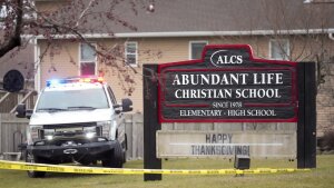 This photo shows a large wooden sign that says "Abundant Life Christian School" on it. An emergency vehicle is parked on the grass next to the sign. Yellow caution tape extends across the photo.