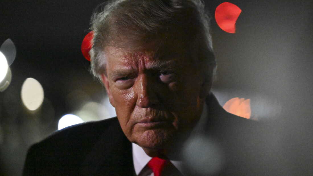 President Trump from the shoulders up in a close-up shot. He is wearing a red tie and black suit.