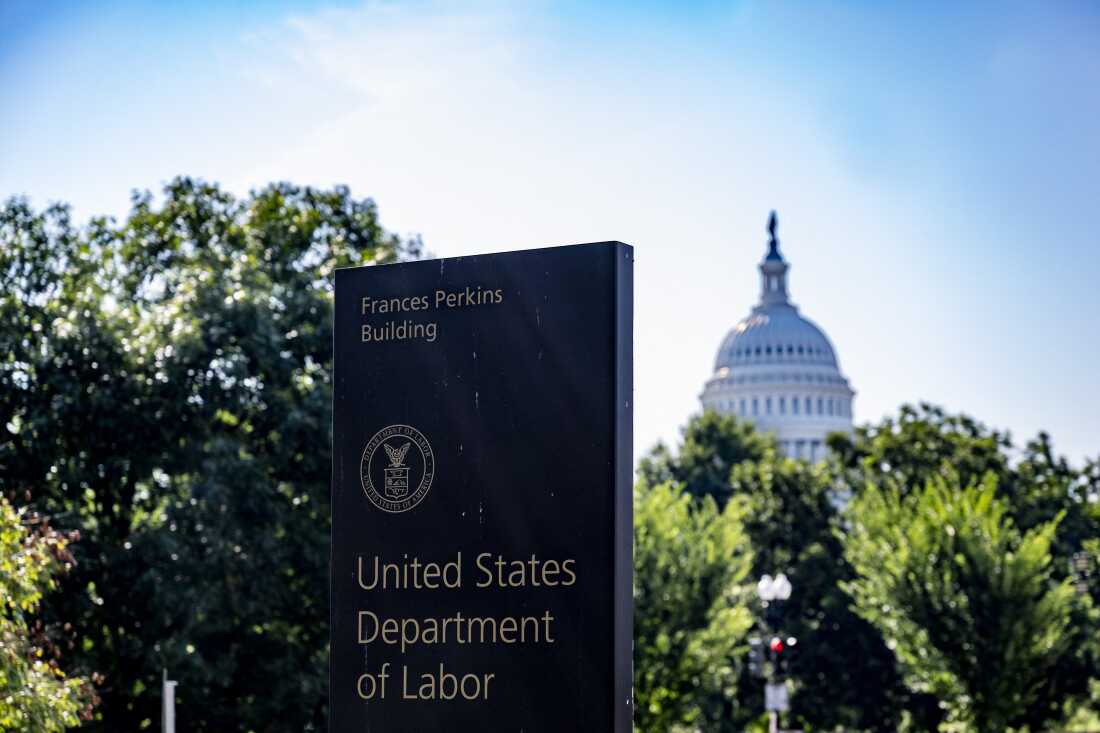 This photo shows a sign saying "Frances Perkins Building" and "United States Department of Labor." The seal of the Labor Department also appears on the sign. The Capitol dome rises in the background.