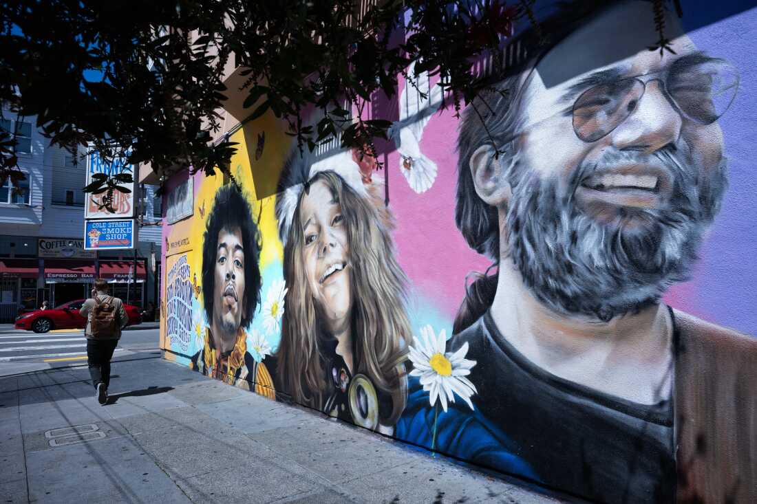 This photo shows a wall mural on the outside of a building in San Francisco’s Haight-Ashbury district. The mural comprises paintings of three hippie-looking people: a man, a woman and another man.
