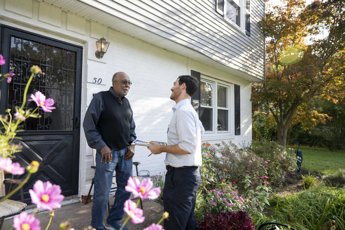 Standing outside the front door of a house, New Haven resident James Fripp Jr. (left) speaks with Eli Sabin.