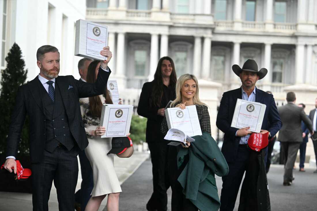 Several conservative commentators and activists hold up white binders outside the White House.