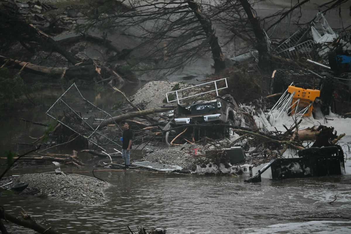 A member of the public stands next to overturned vehicles and broken trees on Saturday after a flash flood at the Guadalupe River in Kerrville, Texas.
