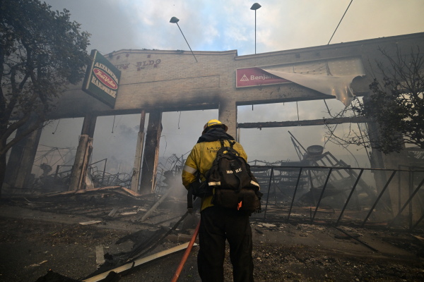 In this photo, a firefighter holding a water hose extinguishes the remains of Altadena Hardware. Only the front facade of the building remains.