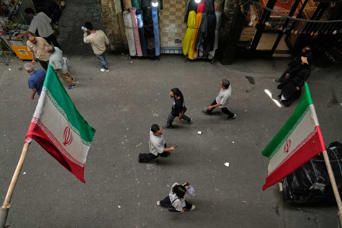 People walk as Iranian flags hang in the Grand Bazaar in Tehran, Sunday, May 3, 2026.