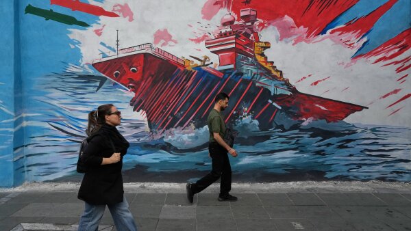 People walk past a mural depicting a U.S. aircraft carrier under missile attack by Iran in downtown Tehran.