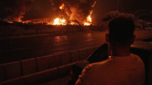 A man looks at flames rising from an oil storage facility after it appeared to have been struck by an Israeli strike in Tehran, Iran, early Sunday, June 15, 2025. 
