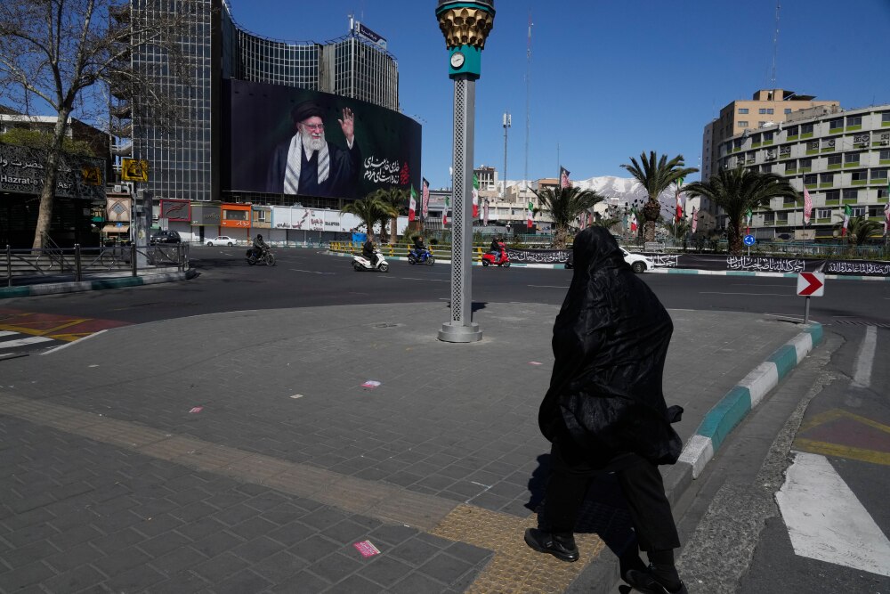 A woman crosses almost deserted square with a billboard at rear showing a portrait of the late Iranian Supreme Leader Ayatollah Ali Khamenei, who was killed in the U.S.–Israeli military campaign, in Tehran, Iran, Tuesday, March 3, 2026. (AP Photo/Vahid Salemi)