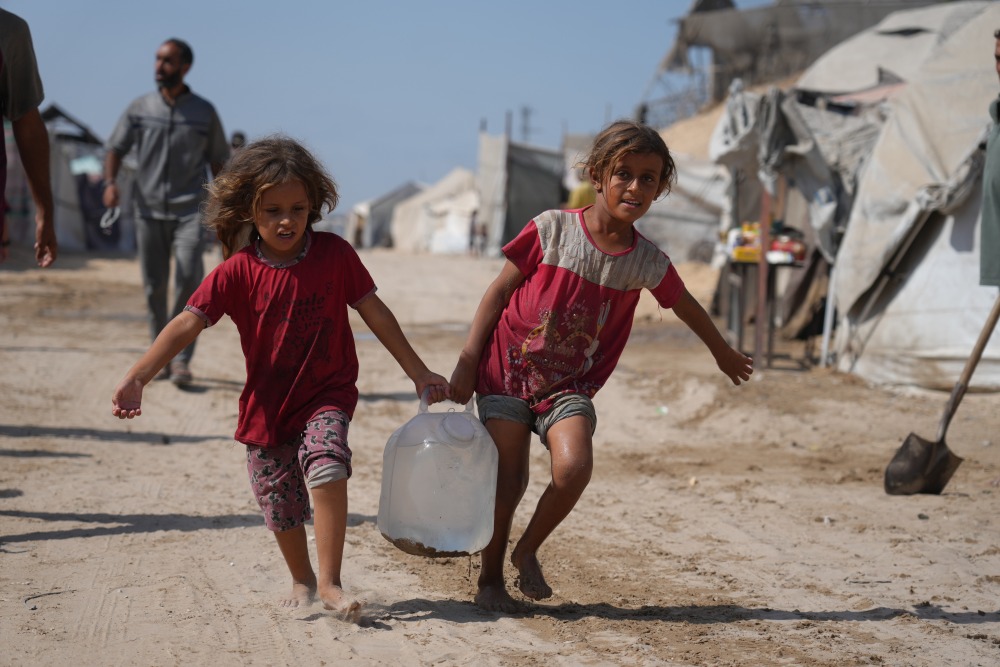 Displaced Palestinians girls carry a jerrycan after collecting water from a distribution point at a tent camp in Muwasi, an area that Israel has designated as a safe zone, in Khan Younis southern Gaza Strip on Monday. (AP)