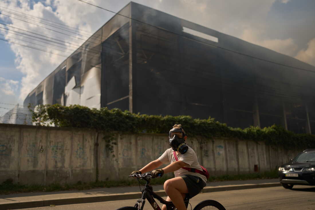 A local resident wears a gas mask as he rides a bicycle past a partially destroyed warehouse after a Russian drone attack in Brovary on the outskirts of Kyiv, Ukraine, Friday, Sept. 4, 2026.