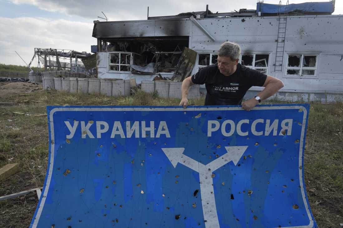 Ukrainian historian Yuri Savchuk, the head of Ukraine's World War II history museum, carries a road sign on Aug. 16 in western Russia's Kursk region, an area captured by Ukrainian troops. The sign reads 'Ukraine' to the left, and 'Russia' to the right.