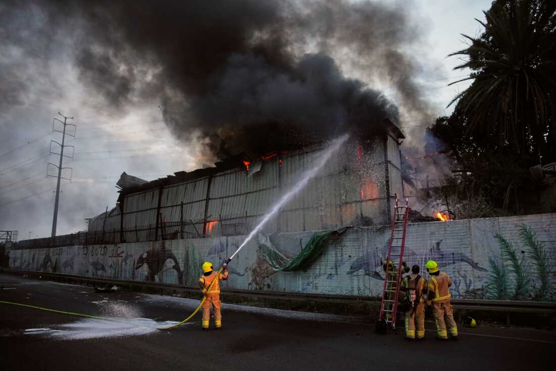 Firefighters try to extinguish flames at the site of a direct hit by an Iranian missile strike in Holon, central Israel, Friday.