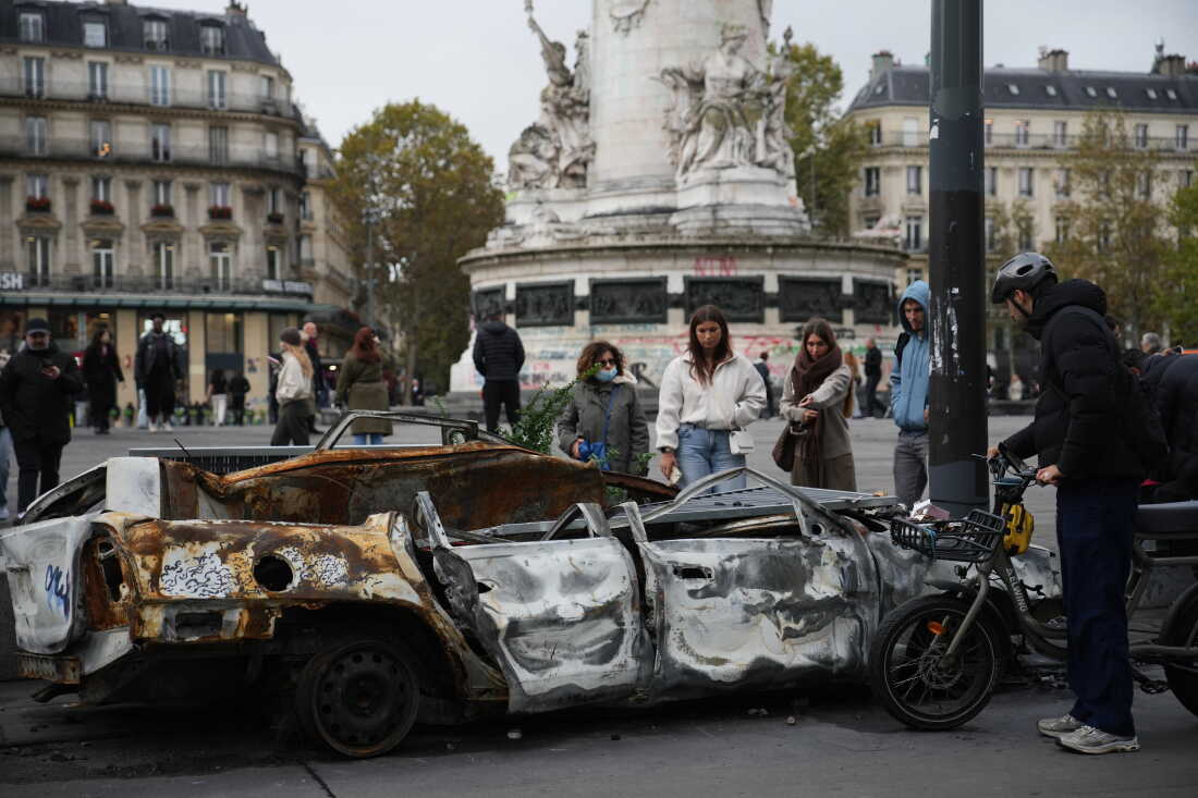 People watch a burned-out car after a quiet night Monday under curfew, the first since weekend protests over the cost of living turned into rioting and looting across France, in Paris, Tuesday, Oct. 20, 2026.