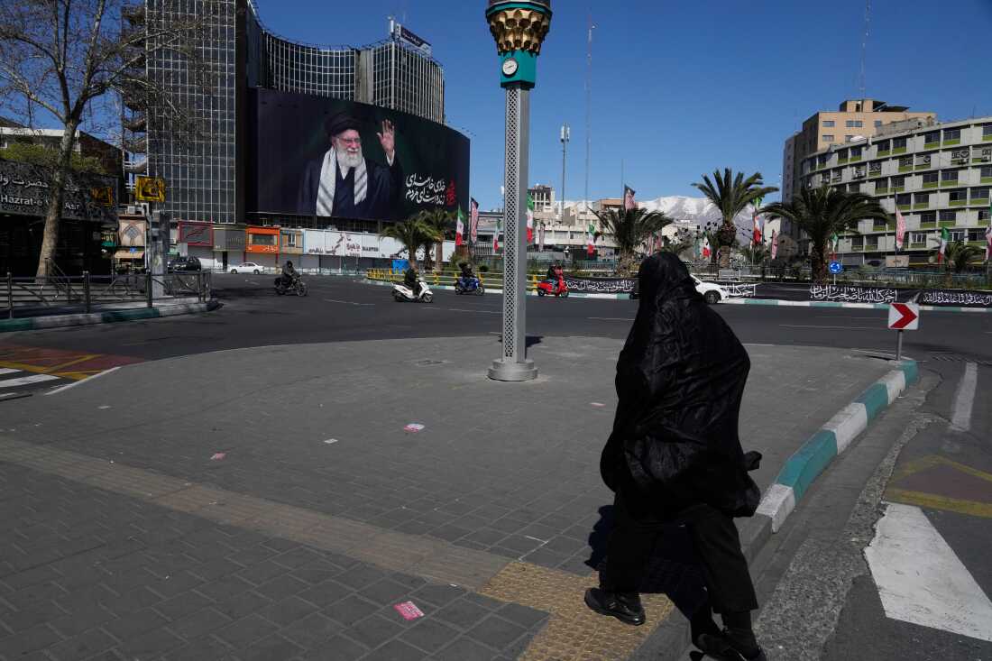 A woman crosses almost deserted square with a billboard at rear showing a portrait of the late Iranian Supreme Leader Ayatollah Ali Khamenei, who was killed in the U.S.–Israeli military campaign, in Tehran, Iran, Tuesday, March 3, 2026. (AP Photo/Vahid Salemi)