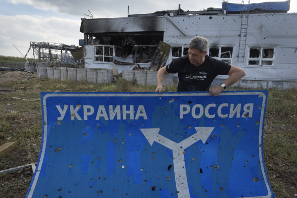Ukrainian historian Yuri Savchuk, the head of Ukraine's World War II history museum, carries a road sign on Aug. 16 in western Russia's Kursk region, an area captured by Ukrainian troops. The sign reads 'Ukraine' to the left, and 'Russia' to the right.