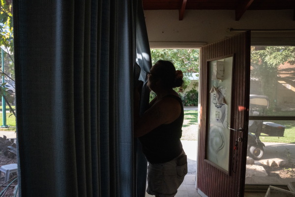 Yasmine Raanan, 56 looks through her curtains the same way she did when she heard loud sounds on October 7th and was able to see a break in the fence with Hamas members streaming in, on Sept. 23, 2024 in Kibbutz Beeri.