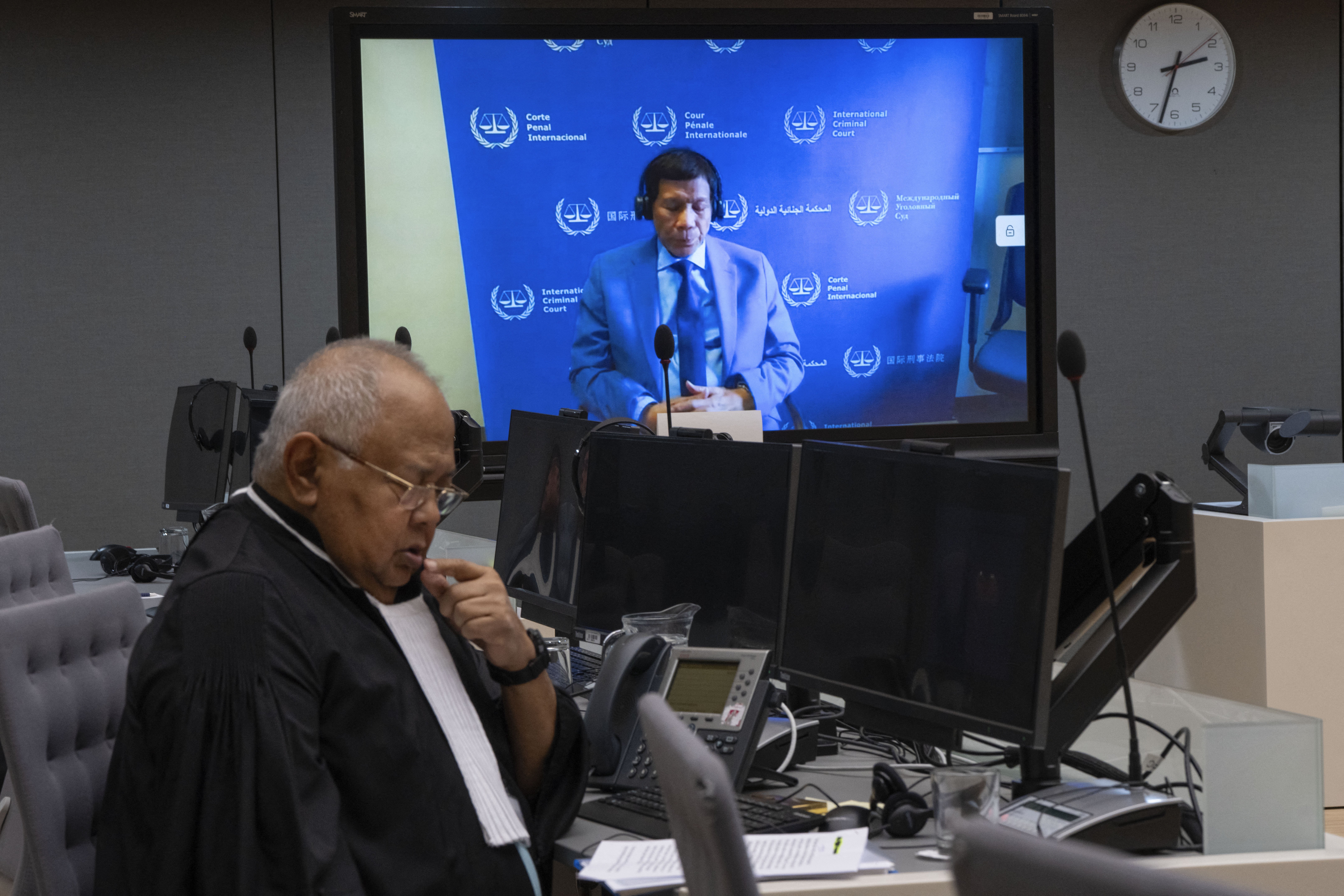 Former Philippine President Rodrigo Duterte is seen on a screen with his lawyer Salvador Medialdea (left) in the courtroom during his first appearance before the International Criminal Court on charge of crimes against humanity over his deadly crackdown on narcotics, in The Hague on March 14.