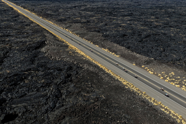 In this aerial photo, triathletes bike on a long straight road that cuts through a rough, black lava field during the Ironman World Championship on October 11, 2025, in Kailua-Kona, Hawaii.