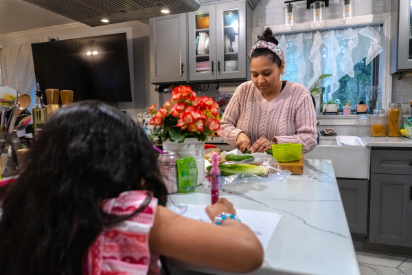 Lusely Martinez cuts vegetables at her kitchen island while her daughter sits at the island and draws.