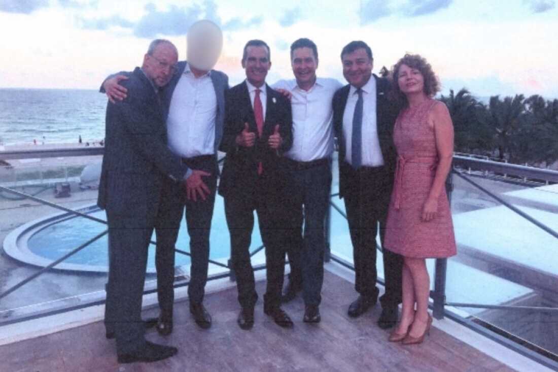 This photo shows Eric Garcetti standing on a hotel rooftop in Miami Beach, Fla., with three people (two men and a woman) to the right and two men to the left. The men are dressed in suits, and the woman is wearing a dress. The man on the far left, Rick Jacobs, has outstretched his hand and placed it in front of the crotch of the man standing between him and Garcetti. This photo shows Eric Garcetti standing on a hotel rooftop in Miami Beach, Fla., with three people (two men and a woman) to the right and two men to the left. The men are dressed in suits, and the woman is wearing a dress. The man on the far left, Rick Jacobs, has outstretched his hand and placed it in front of the crotch of the man standing between him and Garcetti.