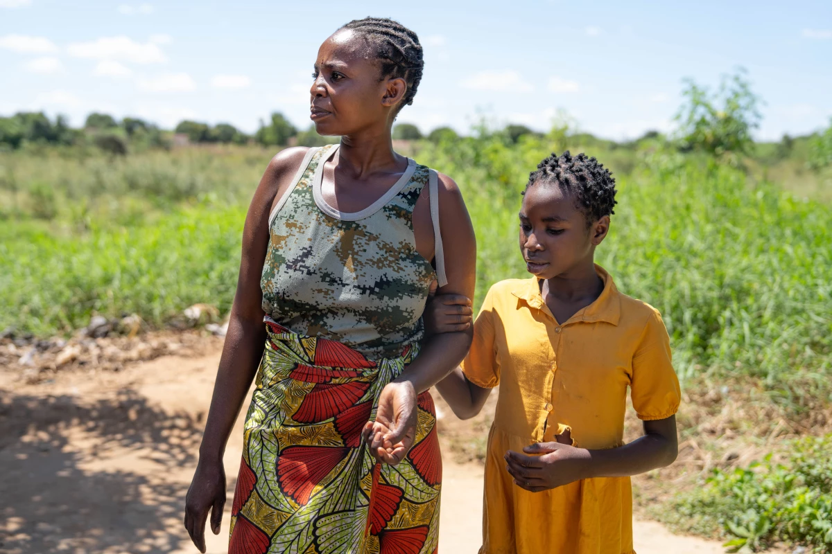 Theresa Mwanza and her daughter, Dorcas, stand in a field near their house. After their USAID-funded clinic closed, Theresa tried to get HIV medications at a government-run clinic but was turned away and told she needed to get 'direction or guidance' from that now-shuttered facility.