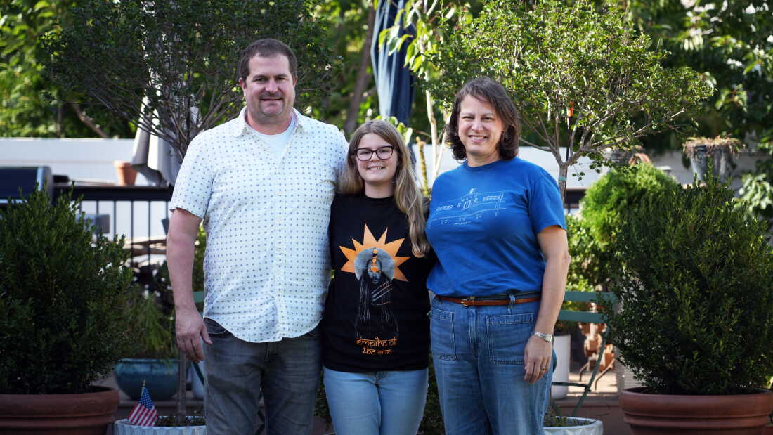 Cora Walsh stands outdoors between her parents, Chris Walsh and Emily Johnson.