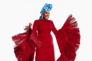 A woman in a dramatic, tassled. floor-length red dress and blue head turban, singing forcefully