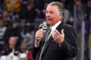   Barry Melrose speaks to fans holding a microphone at an arena