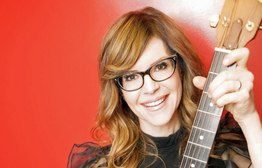 Woman with reddish blonde hair holding up a guitar 