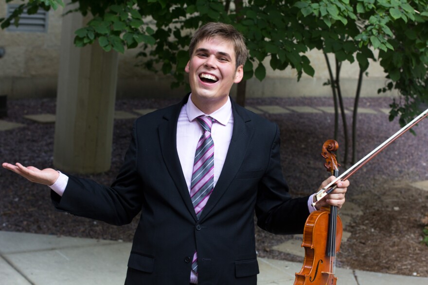 A man with a big smile outstretches his arms, violin and bow in his left hand.