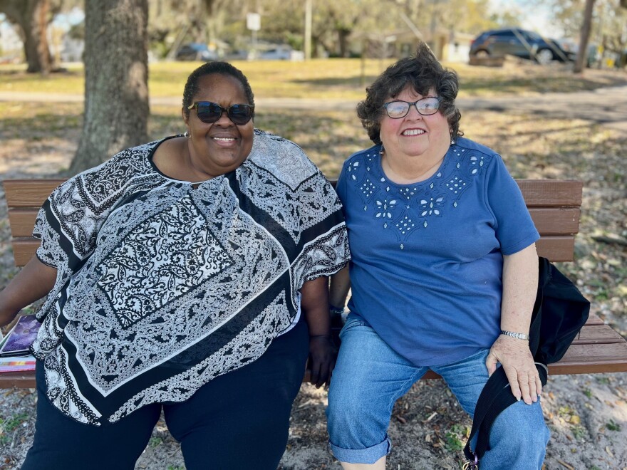 Two older women, Mary Jones and Carita Wells, sit on a park bench in Tampa