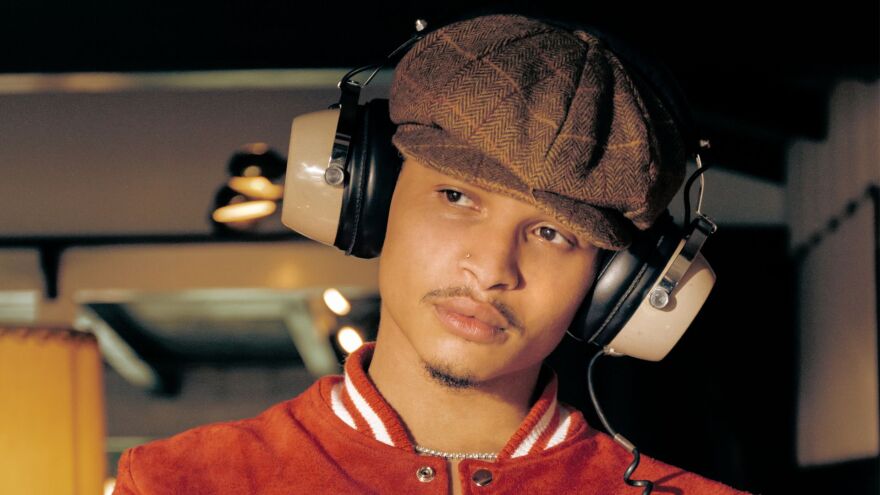 African American man with a goatee wearing hat and headphones looking to the left 