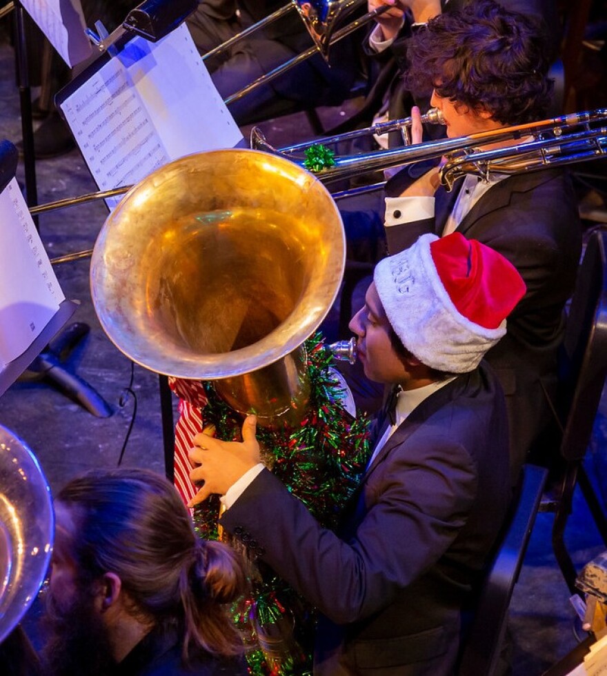 A tuba player wearing a Santa hat; their instrument is wrapped in tinsel