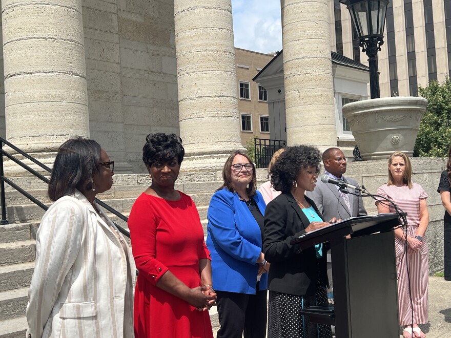 Debbie Watts Robinson stands on the far left of the image, smiling at Montgomery County Commissioner Mary McDonald as Dayton Mayor Shenise Turner-Sloss speaks at a podium