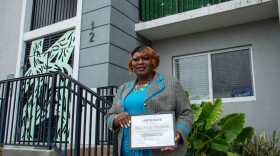 Beatrice Regina Thomas stands in front of the redeveloped Liberty Square, holding a certificate in Entrepreneurship awarded by Related Group and The Miami-Dade Chamber of Commerce.